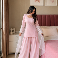 Woman in a pink traditional outfit standing in a bedroom with a bed and dresser.