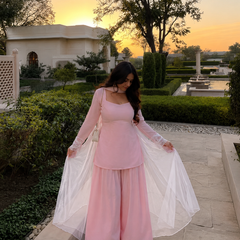 Woman in a pink dress with sheer sleeves standing outdoors during sunset.